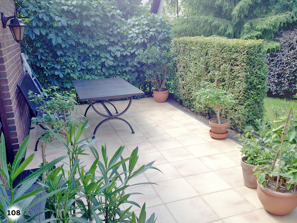 Ein wundervolle Terrasse mit beigen Betonsteinen auf der sich Pflanzen, Tisch und Stühle befinden