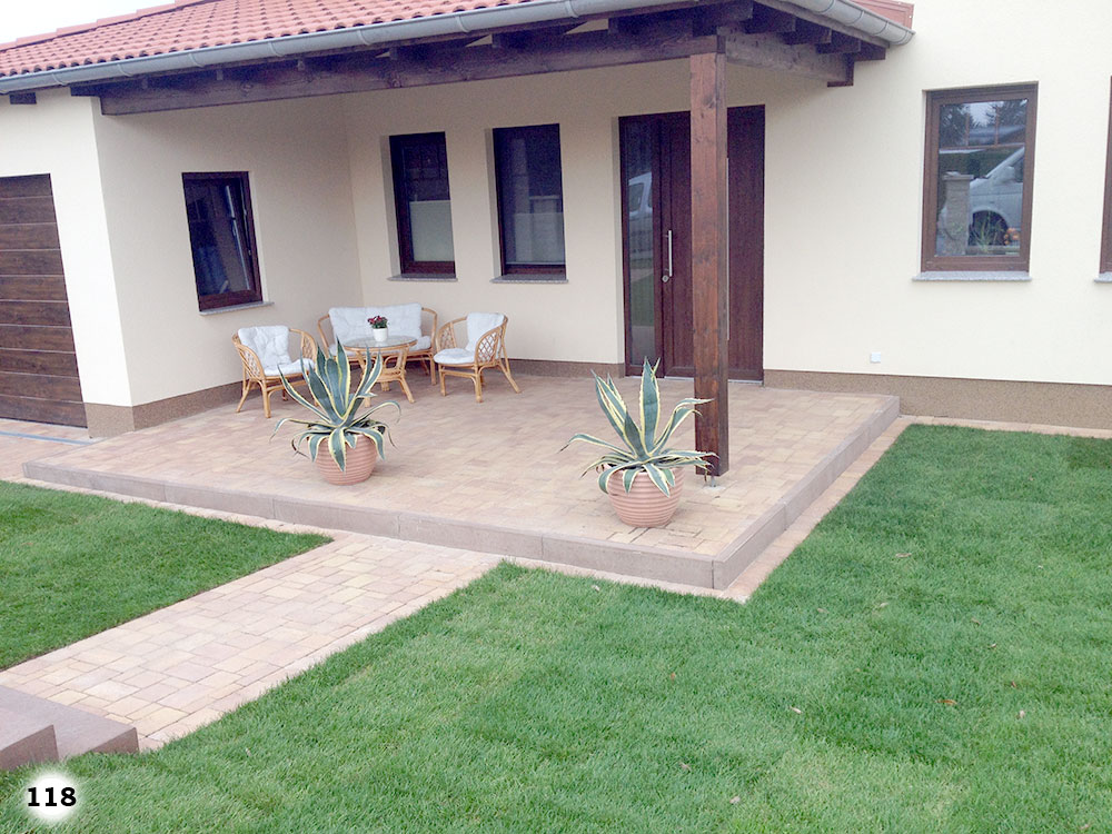 Ein schickes Haus an einer Grünfläche mit einer überdachten Terrasse auf der Pflanzen, Tisch und Stühle stehen