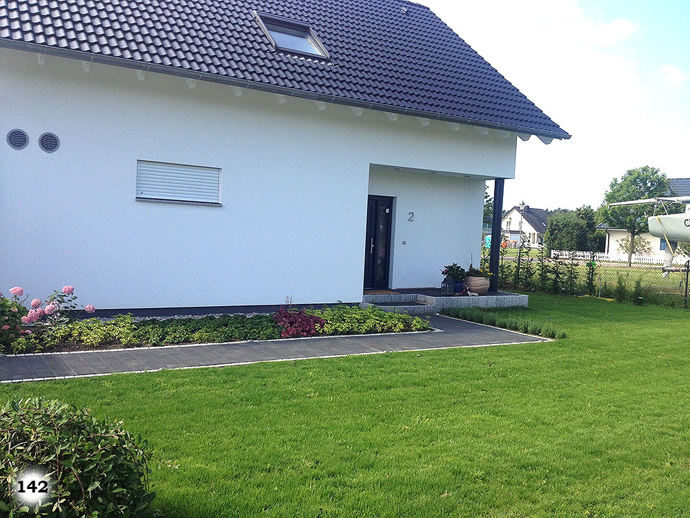 Ein Haus vor einer Grünfläche mit einem Beet und Gehweg vor dem Eingang