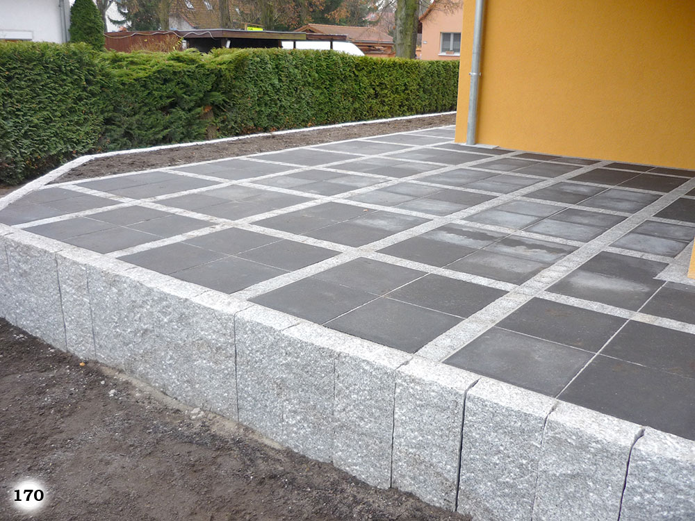 Eine Terrasse aus Betonsteinen welche in Quadraten eingeteilt sind und von grauen Palisaden abgetrennt werden