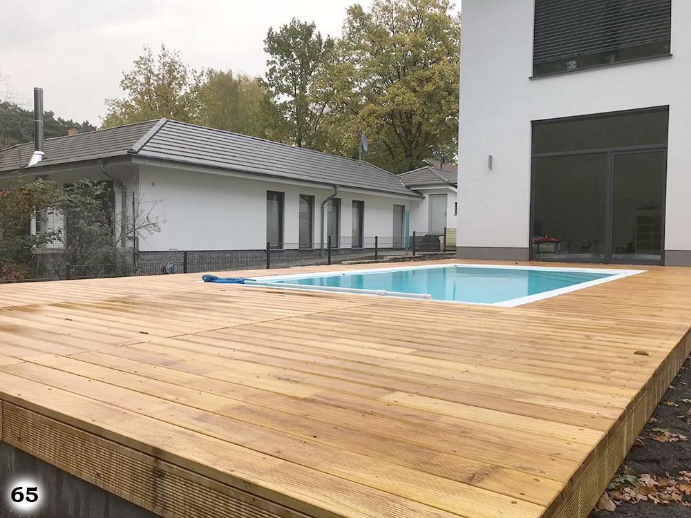 Ein in einem schönen Holzboden eingelassener Pool welcher vor einem weißen Haus steht