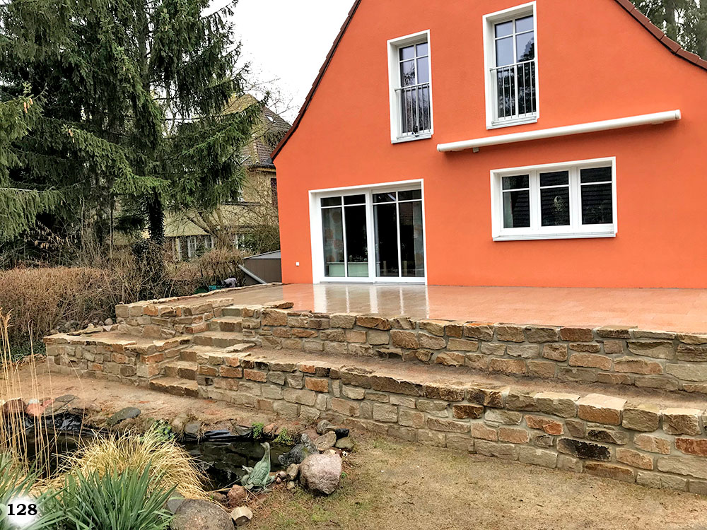 Altwirkendes Mauerwerk mit einer eingelassenden Treppe an einem knall orangen Haus