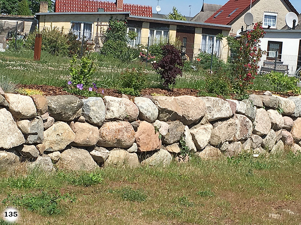 Eine Mauer aus vielen großen Steinen umrandet eine Steigung eines Grundstücks