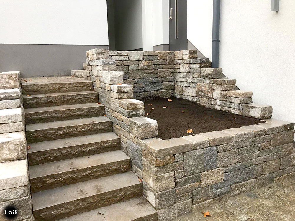 Steinmauer aus verschieden großen Steinen umranden ein Weg und eine Treppe eines Hauseingangs