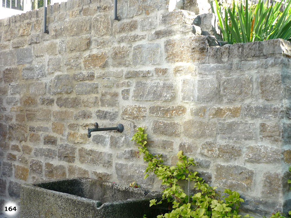 Eine Mauer mit unterschiedlich farbenden und großen Steinziegeln an der sich ein Wasserhahn befindet