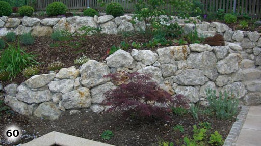Abgeschrägte Mauer mit unterschiedlich großen Steinen an dem sich zwei Beete befinden