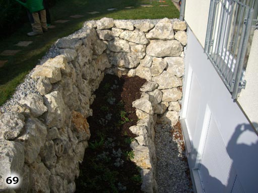 Ein kleines Mauerwerk vor einem eingelassenen Kellerfenster