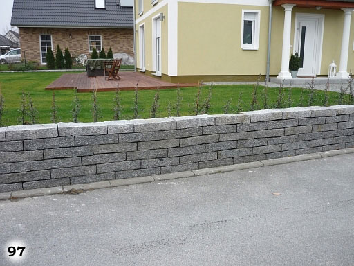 Eine Mauer mit länglichen Steinen vor einem Haus