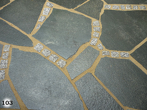 Fläche aus kleinen, hellen, quadratischen Pflastersteinen, mit Mauer aus Pflastersteinen in verschiedenen Brauntönen getrennt