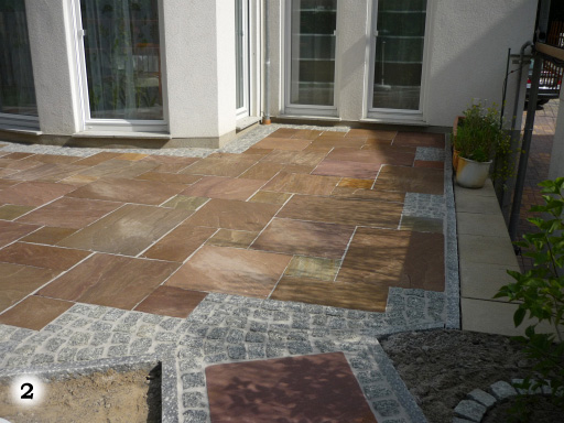 Terrassenfläche aus mittelgroßen braunen Steinplatten und kleinen, grauen, quadratischen Pflastersteinen
