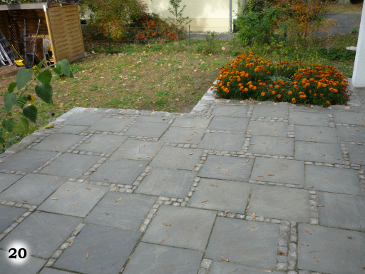 Terrasse aus grauen quadratischen Steinplatten mit kleinen, quadratischen Steinen, verläuft in den Garten