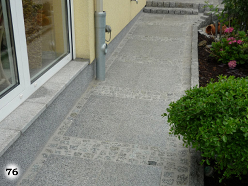 Terrasse aus verschieden großen, dunkel-grauen Steinplatten grenzt an rasenfläche