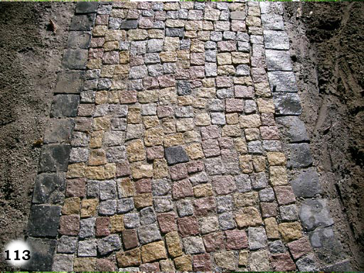 schmaler Weg aus kleinen, bunten, quadratischen Pflastersteinen umsäumt von kleinen, grauen, quadratischen Pflastersteinen