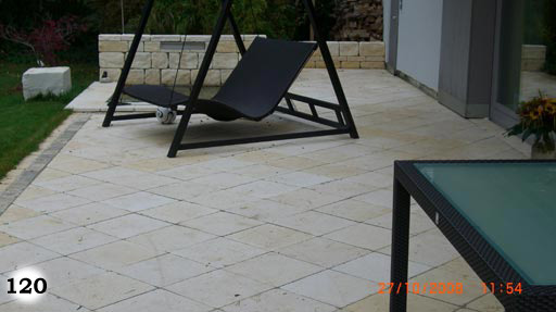 Terrasse aus hellen, quadratischen Steinplatten mit Gartenmöbeln
