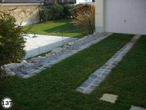 Garageneinfahrt aus Rasenfläche mit zwei Steifen aus je zwei Reihen aus kleinen, bunten, quadratischen Pflastersteinen