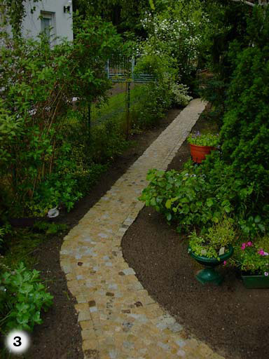 schmaler Weg durch Garten aus kleinen, hellen, quadratischen Pflastersteinen
