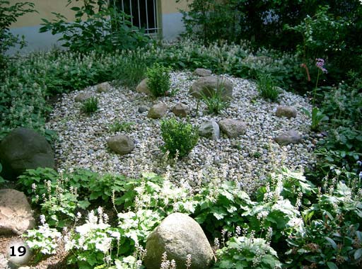liebevoll, wild angelegter Garten mit runder Kiselsteinfläche mit Steinen und kleinen Sträuchern