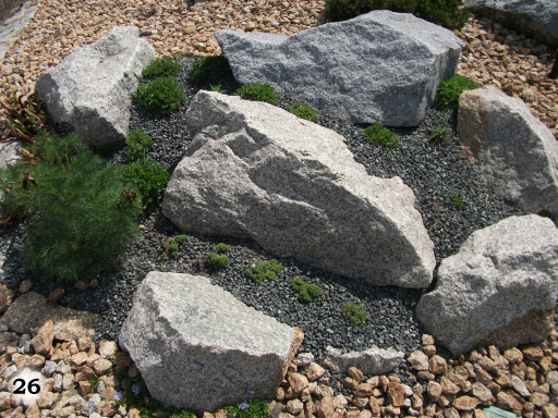 kleine braune Steine um dunkel graue Kieselsteine und große graue Steine mit Moos und kleinen Strauchs