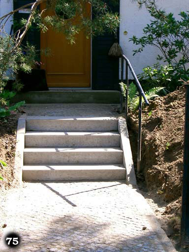 Eine graue simple Treppe an einem Hauseingang mit einem Metallgeländer an der rechten Seite