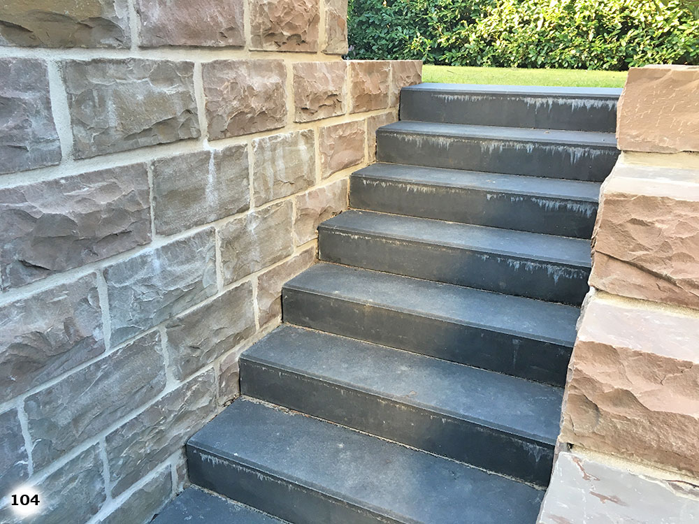 Schwarze Treppe mit kurzen Stufen an einer grauen rauen Mauer