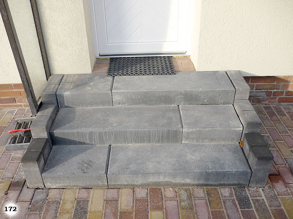 Einfache graue Stufen an einem Hauseingang mit grauen Pflastersteinen an der Seite